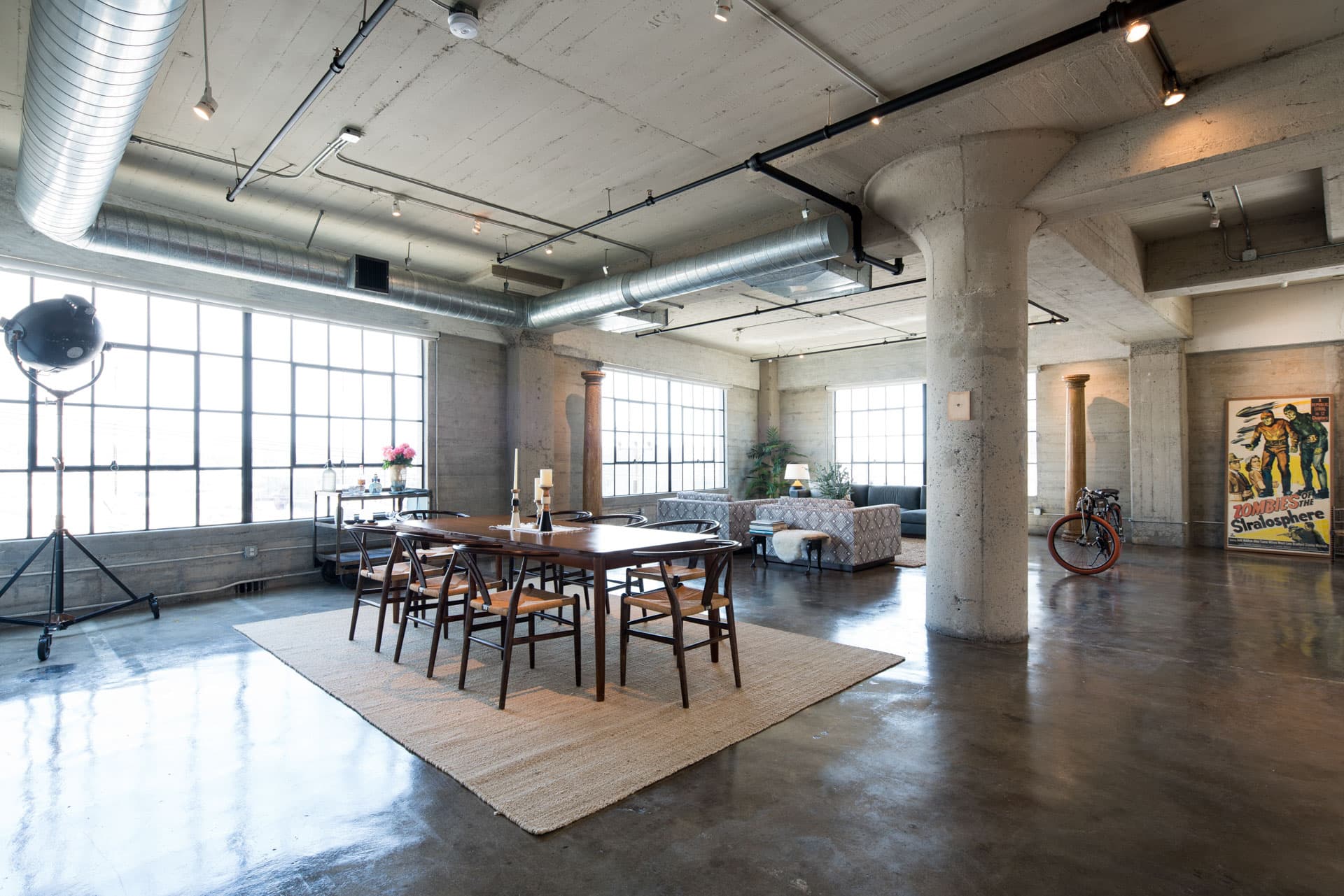 Industrial loft with exposed concrete, steel columns, and mid-century dining setup